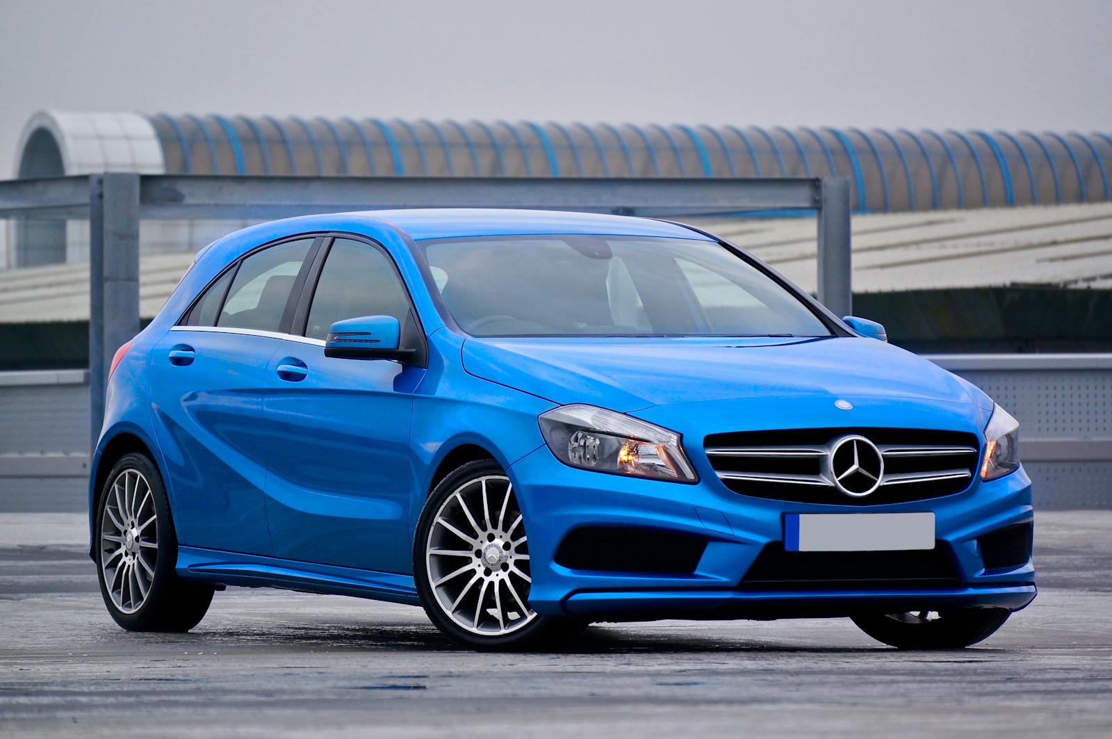 Elegant blue Mercedes-Benz hatchback parked outdoors with a modern architectural backdrop.